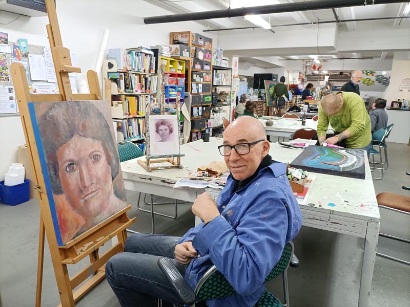 Peter Zlatkoff sits at an easel, where he is painting a portrait of his mother